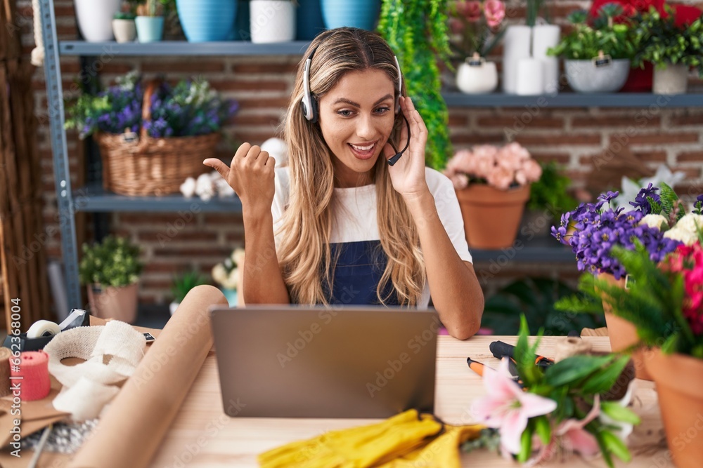 Wall mural young blonde woman working at florist shop doing video call pointing thumb up to the side smiling ha