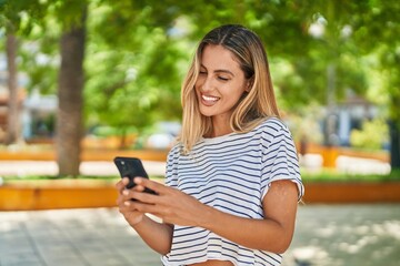 Young blonde woman smiling confident using smartphone at park