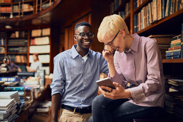 Diverse student duo laughing at a smartphone in a college library