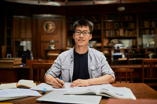 Portrait of a young focused man writing down notes in a university library