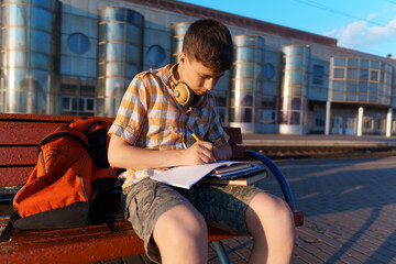a student poses at a railway station, a boy is waiting for a train on the platform, reading books and doing homework, goes to study, the concept of education © soleg