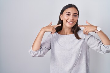 Young hispanic woman standing over white background smiling cheerful showing and pointing with fingers teeth and mouth. dental health concept.