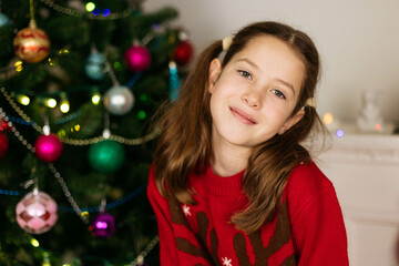 Close-up portrait of a teenage girl against the backdrop of Christmas decorations, smiling and looking at the camera