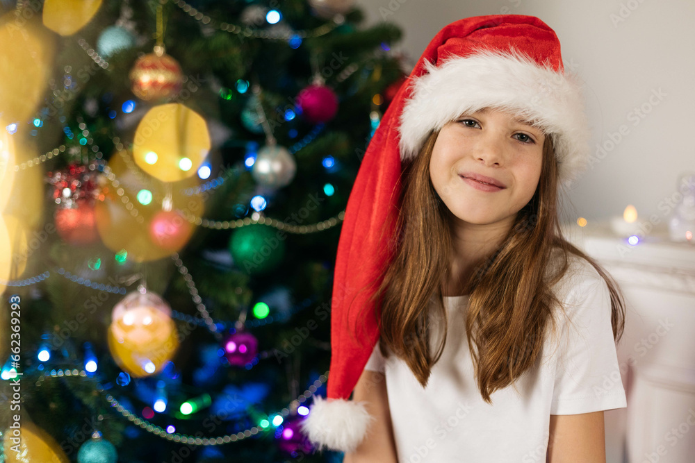 Sticker Close-up portrait of a smiling teenage girl wearing a Santa hat on the background of a Christmas tree, bokeh