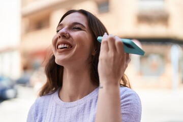 Young woman smiling confident listening audio message by the smartphone at street