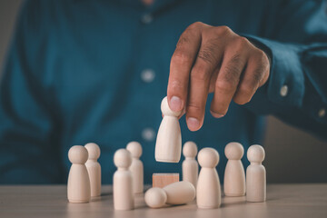 Businessman hand selects a wooden figures human was chosen leadership of teamwork. Concept of...