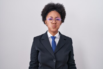 Beautiful african woman with curly hair wearing business jacket and glasses puffing cheeks with funny face. mouth inflated with air, crazy expression. - obrazy, fototapety, plakaty