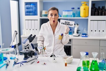Middle age hispanic woman working at eco friendly laboratory scared and amazed with open mouth for surprise, disbelief face