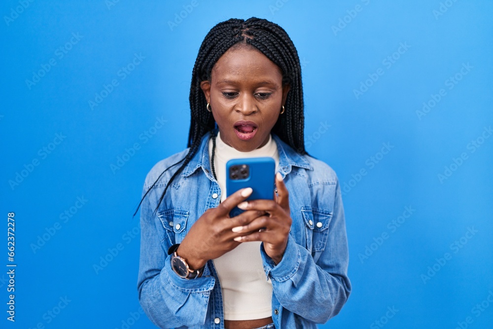 Sticker african woman with braids using smartphone typing message scared and amazed with open mouth for surp