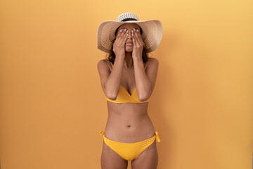 Young hispanic woman wearing bikini and summer hat rubbing eyes for fatigue and headache, sleepy...
