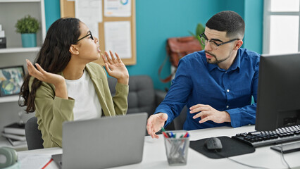 Two office workers, a man and woman, sitting at a table, entangled in a heated argument at their...