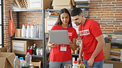 Man and woman volunteers smiling, working on laptop at charity center, standing together in service...