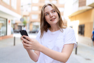 Fototapeta na wymiar Young caucasian woman smiling confident using smartphone at street