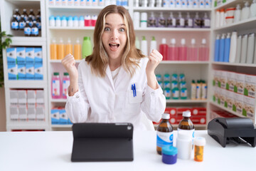 Young caucasian woman working at pharmacy drugstore using tablet screaming proud, celebrating...