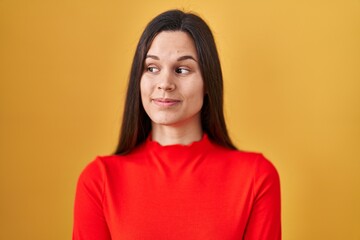 Fototapeta premium Young hispanic woman standing over yellow background smiling looking to the side and staring away thinking.
