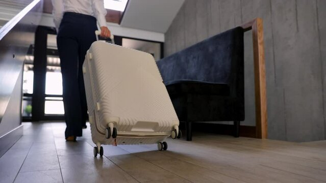 Business woman with travel luggage at the hotel, walking to the doors exit