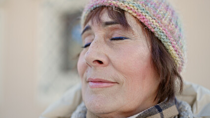 Mature hispanic woman standing with closed eyes at street