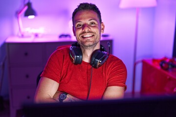 Young hispanic man streamer smiling confident sitting with arms crossed gesture at gaming room