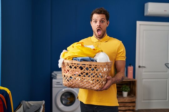 Young hispanic man holding laundry basket afraid and shocked with surprise and amazed expression, fear and excited face.
