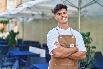 Young hispanic man waiter smiling confident standing with arms crossed gesture at coffee shop...