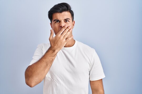 Hispanic man standing over blue background bored yawning tired covering mouth with hand. restless and sleepiness.
