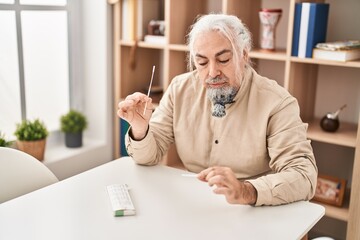 Fototapeta premium Middle age grey-haired man measuring pulse using tensiometer at home