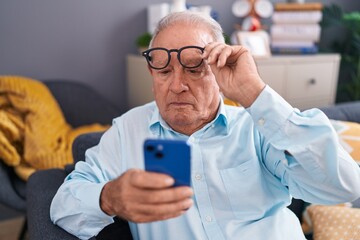 Middle age grey-haired man looking screen smartphone with vision problem at home