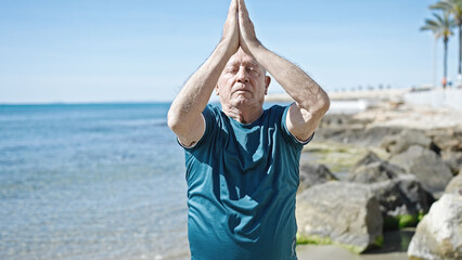 Senior grey-haired man doing yoga exercise at seaside