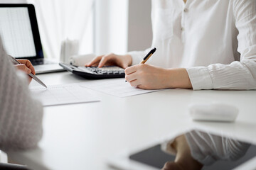 Two accountants using a laptop computer and calculator for counting taxes at white desk in office. Teamwork in business audit and finance