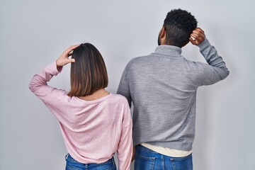 Young hispanic couple standing together backwards thinking about doubt with hand on head