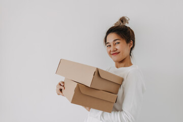 Asian Thai woman holding two parcel brown boxes, deliver gift to someone, smiling and looking the camera isolated on white wall in winter.