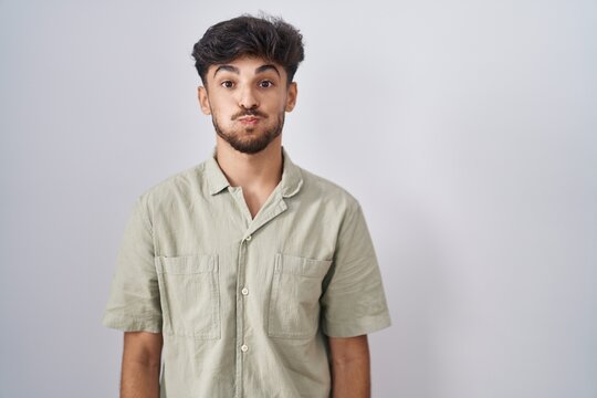 Arab man with beard standing over white background puffing cheeks with funny face. mouth inflated with air, crazy expression.