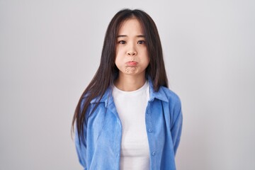 Young chinese woman standing over white background puffing cheeks with funny face. mouth inflated with air, crazy expression. - obrazy, fototapety, plakaty