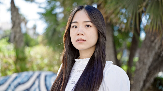 Young chinese woman standing with serious expression at park