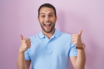 Fototapeta premium Hispanic man standing over pink background success sign doing positive gesture with hand, thumbs up smiling and happy. cheerful expression and winner gesture.