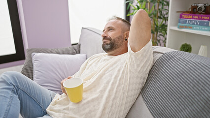 Handsome young man in deep thought, sitting comfortably at home, sipping coffee on a relaxing morning.