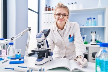Naklejka na ściany i meble Young blonde woman scientist using microscope writing report at laboratory