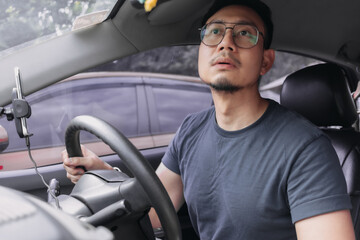 Asian Thai man with beard,  wear eyeglasses and navy t-shirt, parking a car by looking at rear mirror, driving training for safety. pick up girlfriend after work.