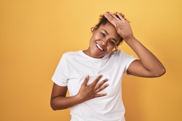 Young hispanic woman with curly hair standing over yellow background touching forehead for illness and fever, flu and cold, virus sick