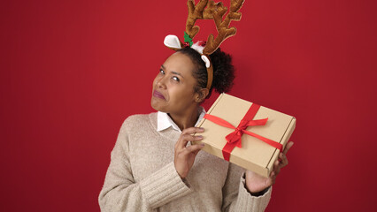 African american woman listening sound christmas gift wearing reindeer ears over isolated red...