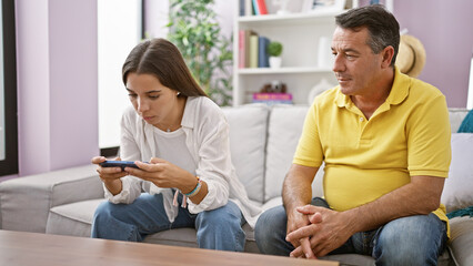 Huddled together at home, father and daughter share a serene indoor moment, sitting on the sofa,...