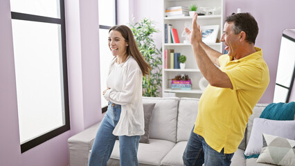 Confident father and smiling daughter joyously dancing together at home, filling their living room with love and happiness