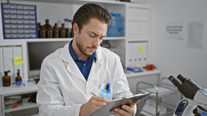 Young hispanic man scientist writing report sitting at laboratory