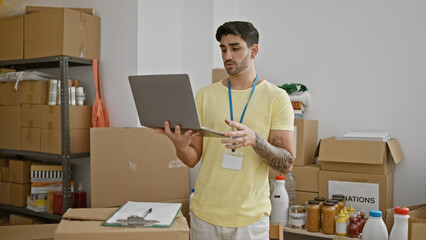 Young hispanic man volunteer using laptop standing at charity center