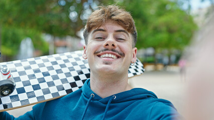 Young hispanic man holding skate make selfie by camera smiling at park
