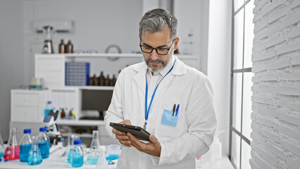 Young hispanic grey-haired man scientist using touchpad at laboratory