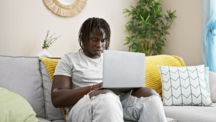 African american man using laptop sitting on sofa at home