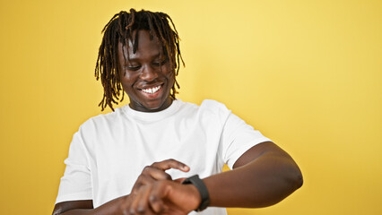 African american man smiling confident looking watch over isolated yellow background