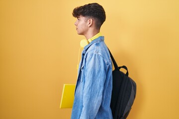 Hispanic teenager wearing student backpack and holding books looking to side, relax profile pose...