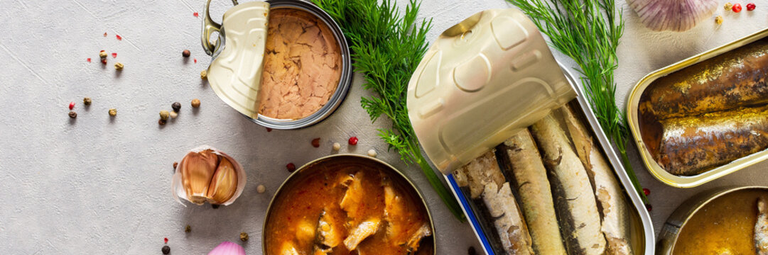 Different open tin cans with canned fish among spices and herbs, canned salmon and mackerel, sprat and sardine, tuna and herring and fish pate, banner